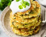 Pile de galettes de courgette dorées, garnies de crème et de coriandre fraîche, sur une assiette en céramique.