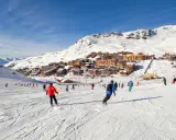 Ośrodek narciarski we francuskich Alpach. Tłumy narciarzy i snowboardzistów na stoku, w tle zabudowania. Francja narty gdzie najlepiej? Tutaj!
