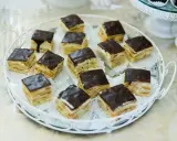 Na białej tacy ułożone są kwadratowe kawałki ciasta z delicjami, polane czekoladą.