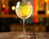 Erfrischender Martini Bianco Spritz mit Zitrone und Minze auf einem Holztisch, im Hintergrund unscharfe Lichter.