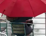 Person under röd paraply på en båt, omgiven av brusande vatten. En typisk bild av bergen regndagar.