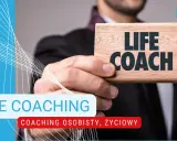 Mężczyzna trzyma tabliczkę z napisem "LIFE COACH". To ktoś, kto wspiera w rozwoju osobistym i życiowym.