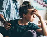 Una donna pensierosa, con una mano sulla fronte, riceve un gesto di conforto. Potrebbe riflettere sull'attaccamento evitante e la sessualità.