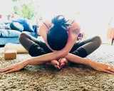 En kvinna i en djup yogaställning på en fluffig matta, omfamnar sig själv i en gest av nonduality.