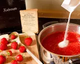Zucker wird zu Erdbeeren in einem Topf gegeben, um zu erfahren, wann wird Marmelade fest. Alte Kochbücher liegen daneben.
