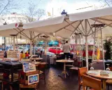 Terrasse d'un restaurant à Barcelone, avec des tables, des parasols, des chauffages d'extérieur et des panneaux indiquant des plats typiques espagnols.