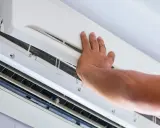 Main d'un technicien ouvrant un climatiseur pour vérifier l'eau et le filtre.