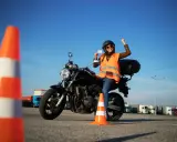 Szczęśliwa motocyklistka z prawem jazdy kategorii A3 w ręku, siedząca na motocyklu, świętuje sukces na placu manewrowym.