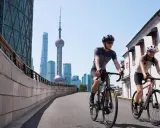 Dwóch rowerzystów w kaskach przemierza miasto, mijając nowoczesne wieżowce i tradycyjną architekturę. Różne rodzaje bębenków rowerowych pozwalają na płynną jazdę.