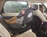 Bebé sonriente en silla de coche a contramarcha, viajando segura mientras mamá conduce.