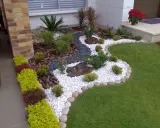 Un jardin moderne avec des graviers blancs, des plantes vertes et des roches. Une belle idee jardin deco pour un extérieur soigné.