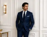 A man in a sharp, navy pinstriped tuxedo stands confidently, hands in pockets.