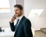 Mężczyzna w garniturze rozmawia przez telefon, jego wyraz twarzy sugeruje, że nastąpiła **zmiana głosu podczas rozmowy**.