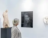A woman views a collection of art, including a wooden sculpture and a portrait, appreciating art as an asset class.