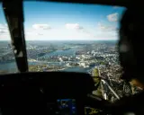 Vy från en helikopter över Stockholm. Staden breder ut sig vid vattnet under en klarblå himmel med moln.
