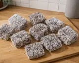 Pyszne kokosanki stary przepis, ułożone na desce. Czekoladowe ciasto oblane wiórkami kokosowymi.