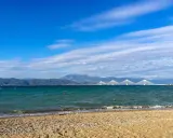Spokojne morze i plaża w Grecji w styczniu. W oddali widać most Rio-Antirio i góry.