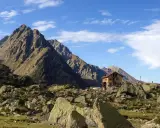 Il rifugio Genova, incastonato tra imponenti montagne rocciose e un cielo azzurro punteggiato di nuvole, offre un riparo solitario e suggestivo.