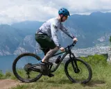 Mężczyzna w kasku jedzie na rowerze MTB po górskim szlaku. Widok na jezioro i miasto w oddali.