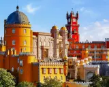 Buntes Sintra Pena Palace mit gelben und roten Türmen, einer blauen Kuppel und einem Uhrenturm unter blauem Himmel.