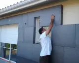 Un ouvrier pose des panneaux d'isolation extérieure en fibre de bois gris.