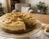 Pyszny sernik z bananami, udekorowany plasterkami owoców i cynamonem, kusi na paterze. Obok kawałek na talerzyku.