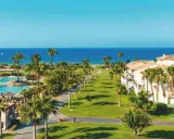 Traumhafter Blick auf das Granada Meer, Palmen säumen den Weg zum Pool und den weißen Hotelgebäuden.