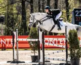 Greta Busacker und ihr weißes Pferd überwinden eine Hürde. Im Hintergrund eine digitale Anzeigetafel.