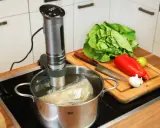 Sous vide garen: Ein Stab im Wasserbad, daneben frisches Gemüse auf einem Holzbrett. Perfekt für zarte Ergebnisse.