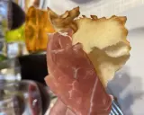 Fetta di gnocco fritto con prosciutto crudo, un classico dei piatti tipici Parma, accompagnato da vino rosso.