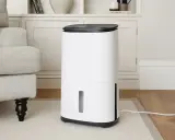 Un deshumidificador blanco moderno junto a un sillón gris, ideal para saber como elegir un deshumidificador y mejorar el ambiente de tu hogar.