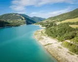 Splendido **lago di Fiastra** con acque turchesi, circondato da colline verdi e case sparse. Un paesaggio sereno e incantevole.