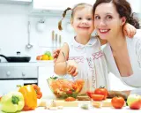 Mama i córka przygotowują sałatkę. W kuchni widać warzywa, oliwę i chleb. To zdrowa żywność, bogata w oligosacharydy, które wspierają florę bakteryjną.