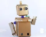 Uroczy robot z kartonu, z oczami-sensorami i kolorowymi kablami, gotowy do nauki i zabawy.