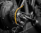 Zestaw do konwersji roweru: czarna piasta z logo, kasetka Shimano, pomarańczowy przewód i przerzutka.