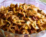 Pyszna sałatka z kurczakiem i makaronem farfalle, kukurydzą i suszonymi pomidorami, posypana natką pietruszki.