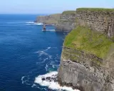Majestatyczne klify Irlandii wznoszą się nad błękitnym oceanem. Zielone zbocza kontrastują z szarymi skałami, tworząc zapierający dech w piersiach krajobraz.