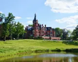 Imponujący pałac z wieżą, jeden z pięknych zamków w Wielkopolsce, otoczony zielenią i stawem.
