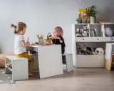 Uroczy kącik dla dziecka w salonie. Dwie dziewczynki rysują przy białym stoliku, otoczone pluszakami i książkami.