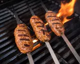 Drei saftige Seekh Kebabs brutzeln auf dem Grill über offenem Feuer.