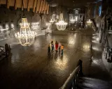 Grupa turystów w podziemnej kaplicy Kopalni Soli w Wieliczce, oświetlonej kryształowymi żyrandolami.