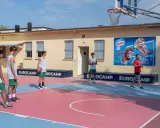 Ragazzi in tenuta sportiva giocano a basket in un camp estivo a Cesenatico, con un cartellone pubblicitario di gelati Motta sullo sfondo.