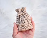 Monedero de ganchillo beige con cordón, sostenido en una mano sobre fondo blanco peludo.