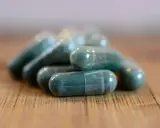 Pile di capsule verdi su un tavolo di legno. Si possono prendere due antibiotici insieme, ma sempre sotto controllo medico.