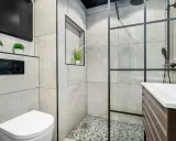 Mampara de ducha con diseño de ventana, separando el espacio de la ducha. Baño moderno con inodoro y lavabo.