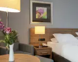 Ein Hotelzimmer mit Bett, Nachttischlampe, Sessel und Blumenstrauß.