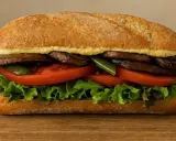 Un delicioso sandwich saludable con champiñones portobello, tomate, lechuga y pimientos verdes en pan rústico.