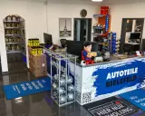 Autoteile-Shop mit Theke, Regalen voller Autoteile, einem Superman-Aufsteller und Fußmatten.