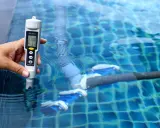 Mano mide salinidad de piscina con cloración salina. El medidor muestra 3160 ppm, indicando posibles problemas.