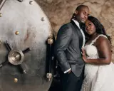 A groom in a patterned tuxedo jacket stands beside a vintage vault door. The father of the bride wears a sharp, dark suit with a satin lapel.